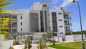 A modern multi-story building with balconies, a covered outdoor area, and a well-maintained lawn. - White Shells Luxury Apartments (Marcoola)