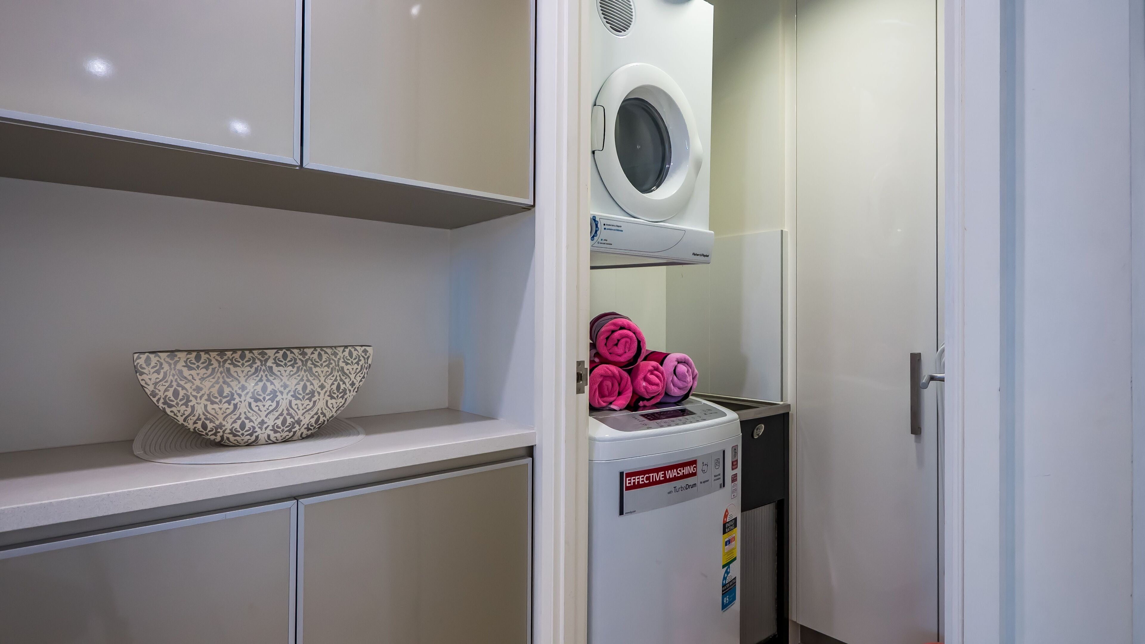 A laundry room with a washing machine, a bowl, and neatly rolled towels.
