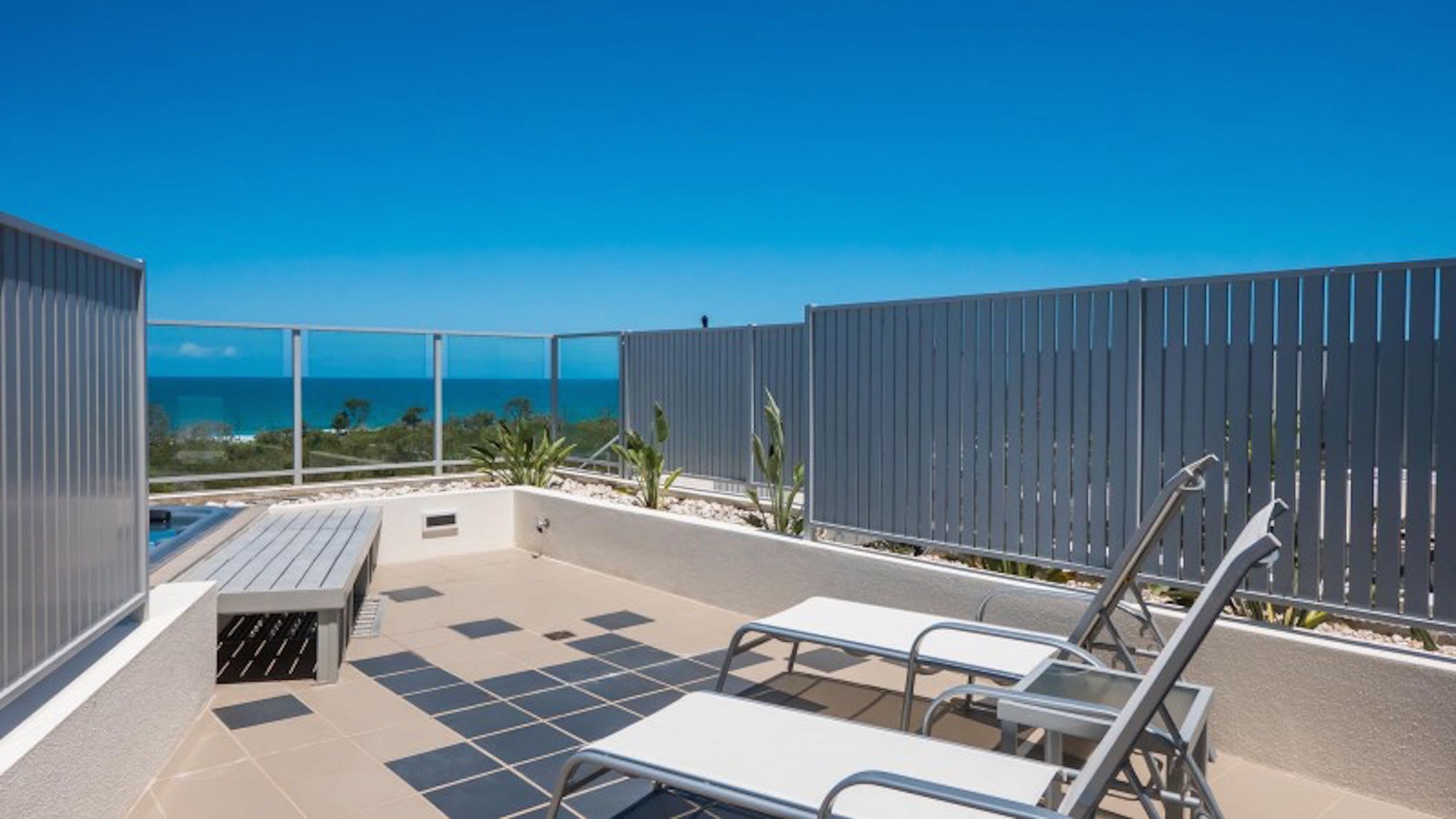 A rooftop terrace with a pool, lounge chairs, and a view of the ocean.