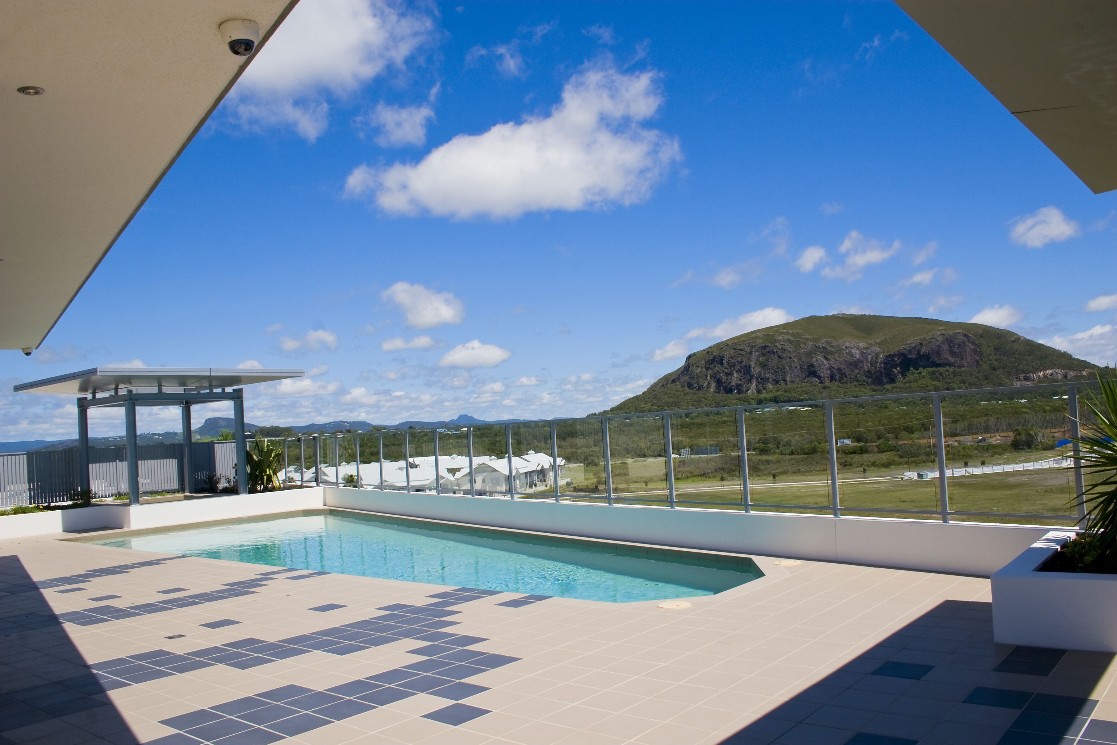 A swimming pool with a view of a mountain, a covered seating area, and a fenced outdoor space.