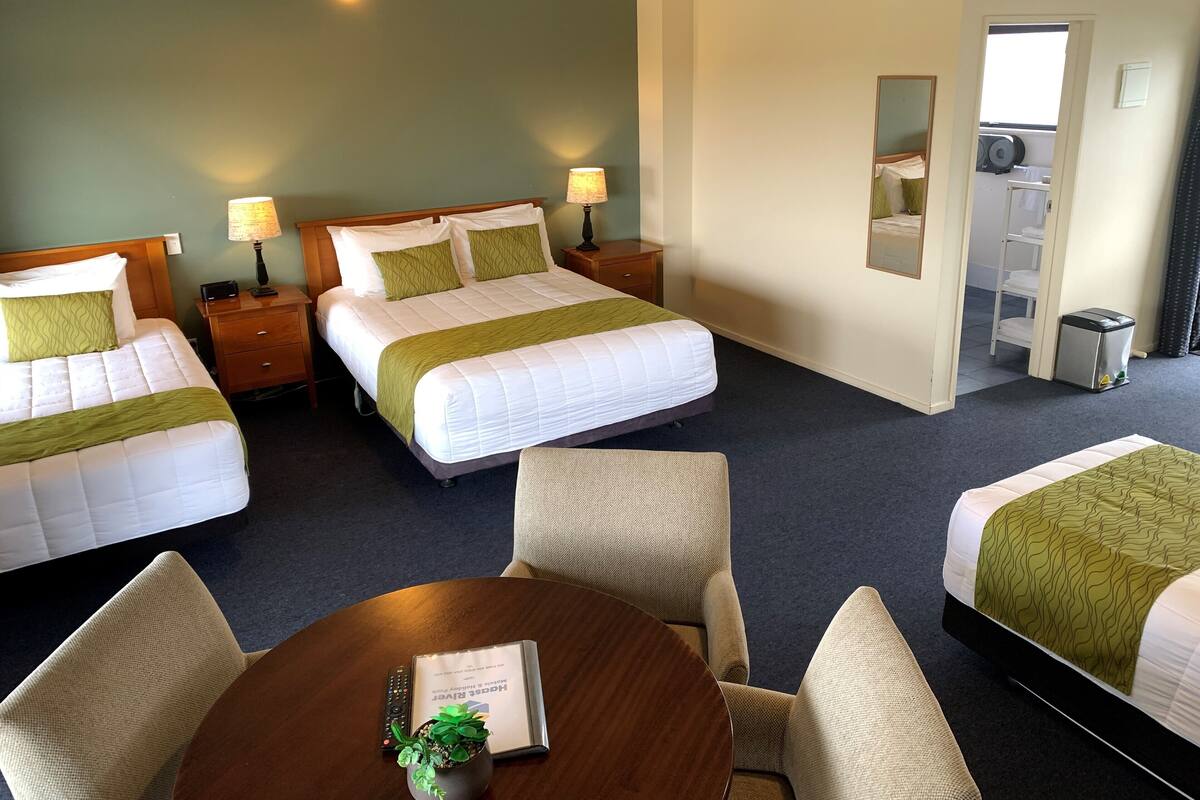A hotel room with two beds, a dining table, and a small mirror.