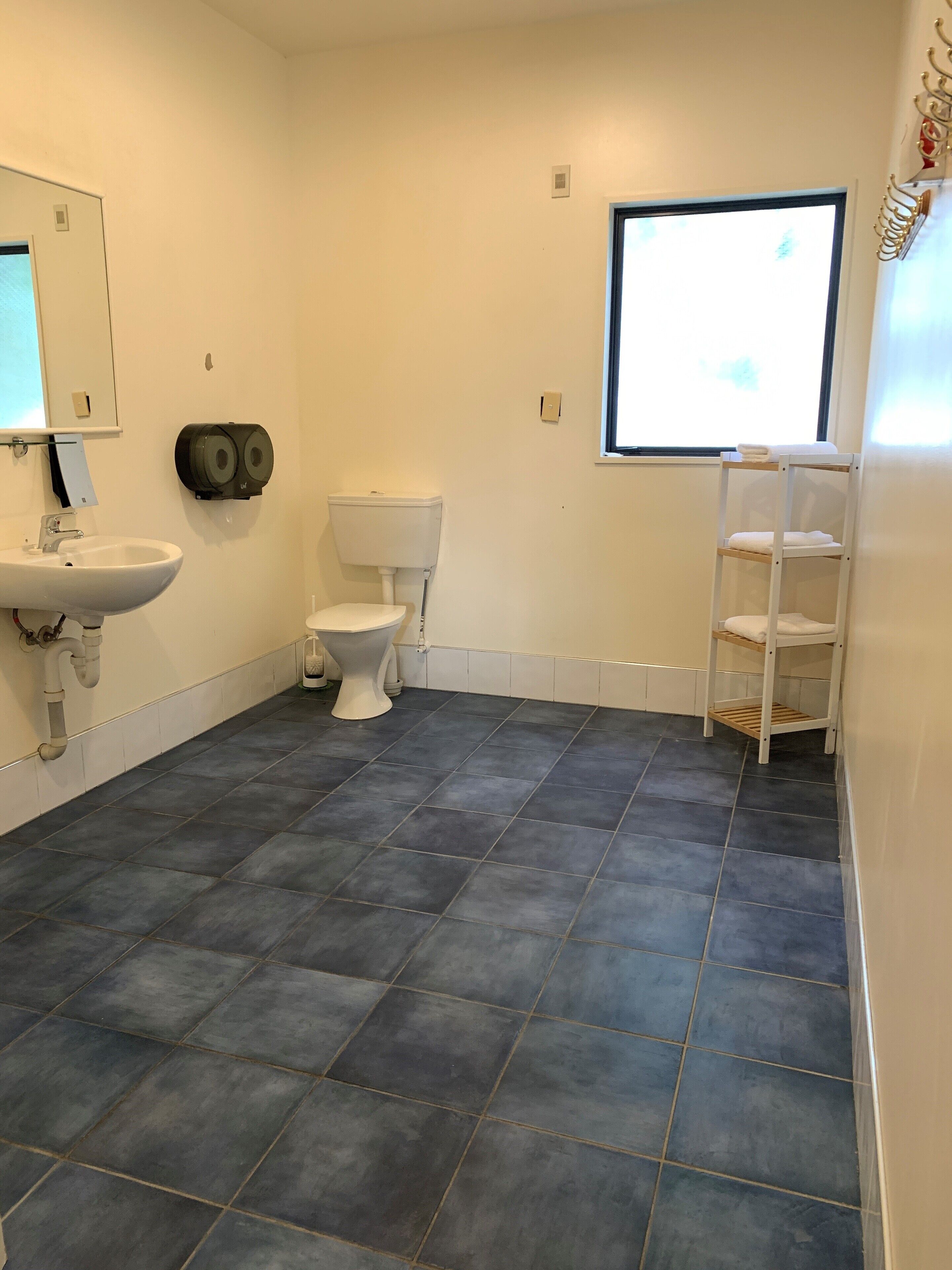 A bathroom with a white sink, toilet, and a shelf with towels.
