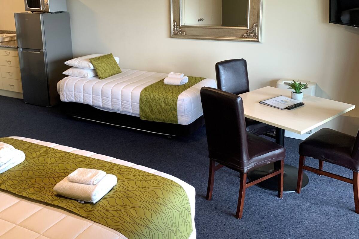A hotel room with two beds, a desk, chairs, a television, and a mirror.