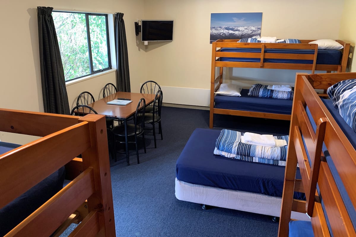 A room with bunk beds, a desk, chairs, a TV, and a window with curtains.