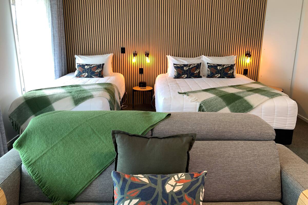 A hotel room with two beds, a sofa, and a wall with vertical slats.