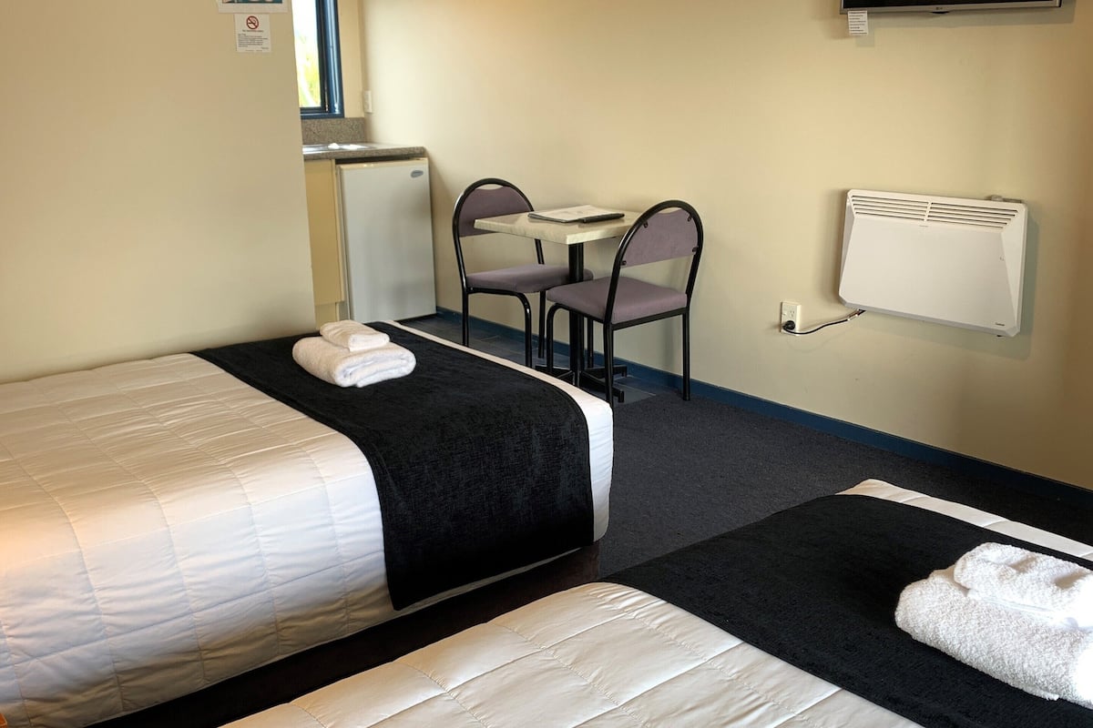 A hotel room with two beds, a small table with chairs, a television, and a radiator.