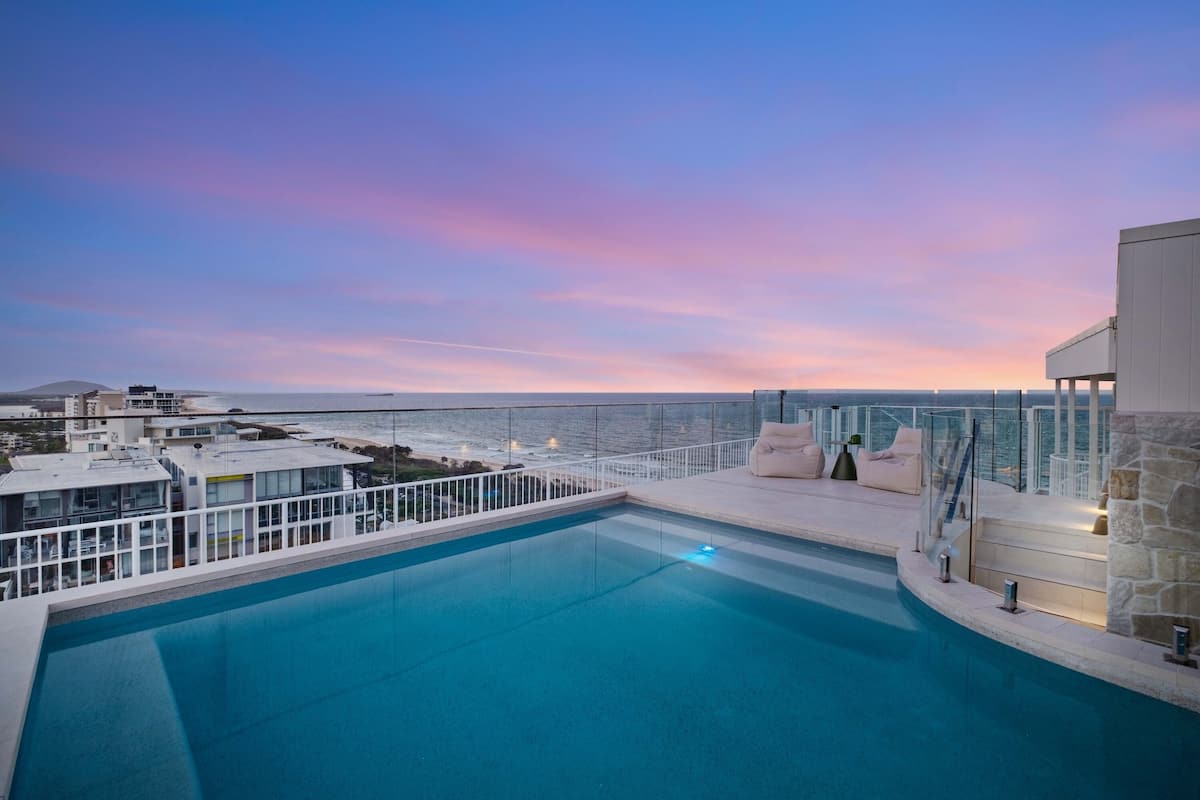 A rooftop pool with a view of the ocean and a sunset.