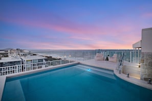 A rooftop pool with a view of the ocean and a sunset.