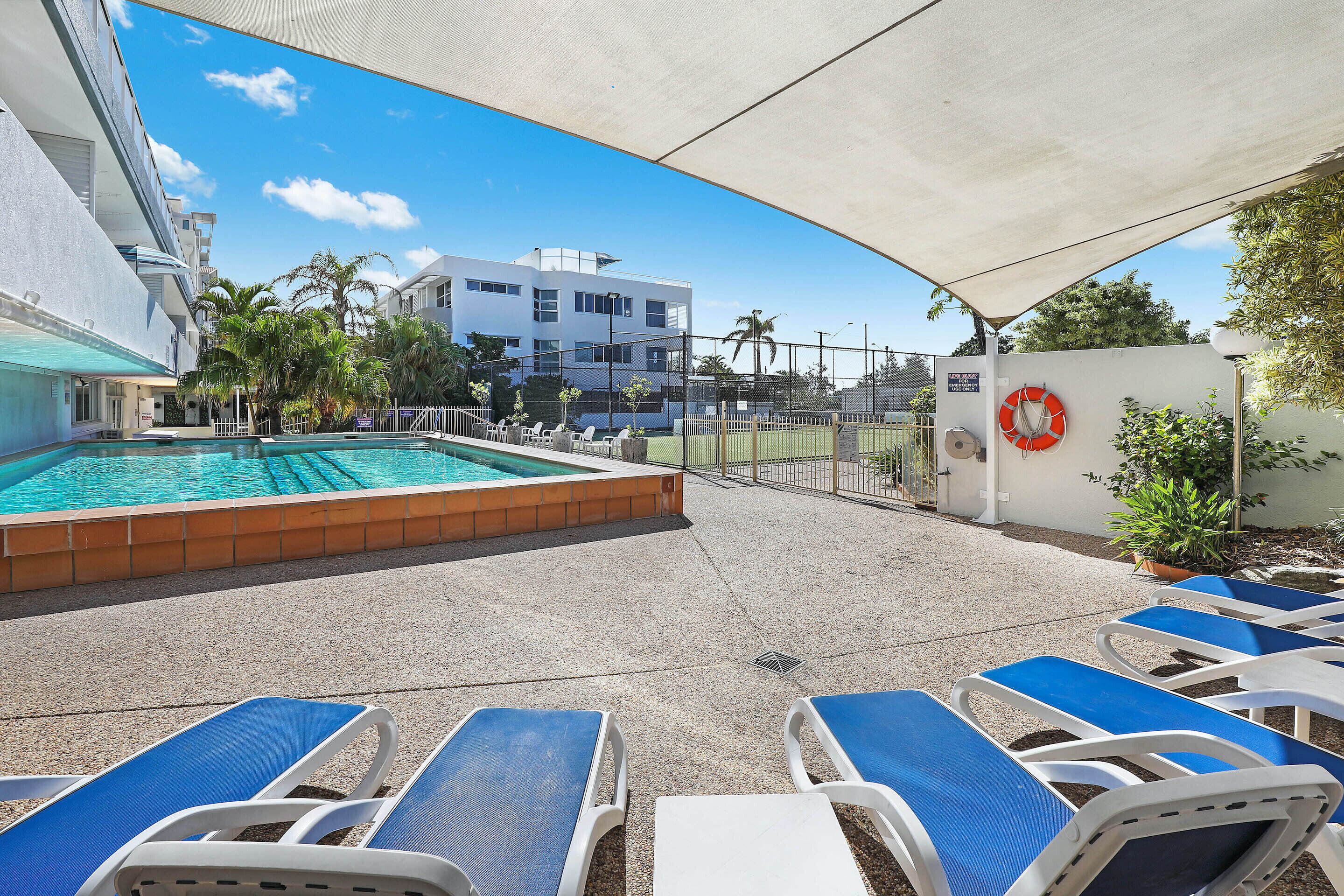 A pool area with lounge chairs, a lifebuoy, and a building in the background.