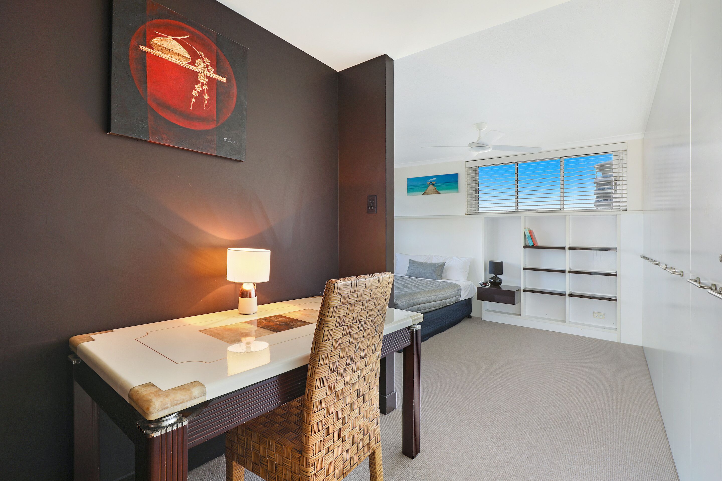 Una habitación de hotel moderna con zona de comedor, cama con vistas y estantería empotrada.