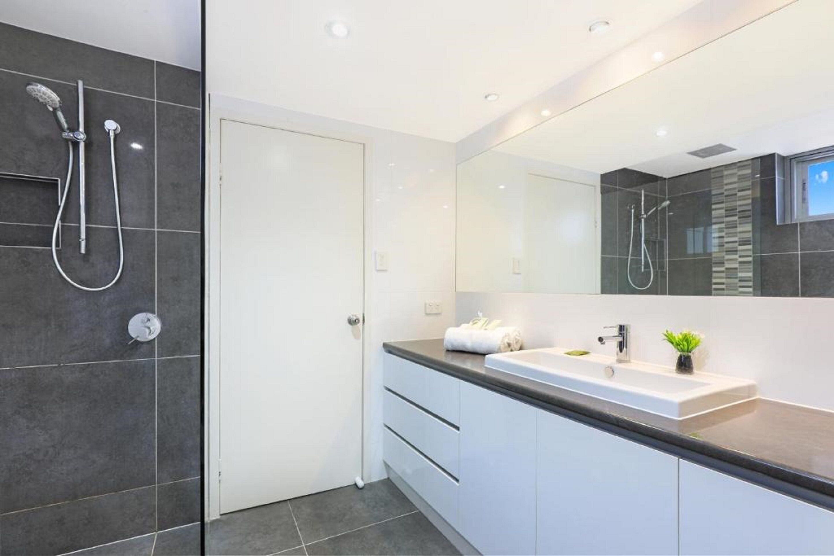 A modern bathroom with a large mirror, a sink, and a shower with two handheld showerheads.