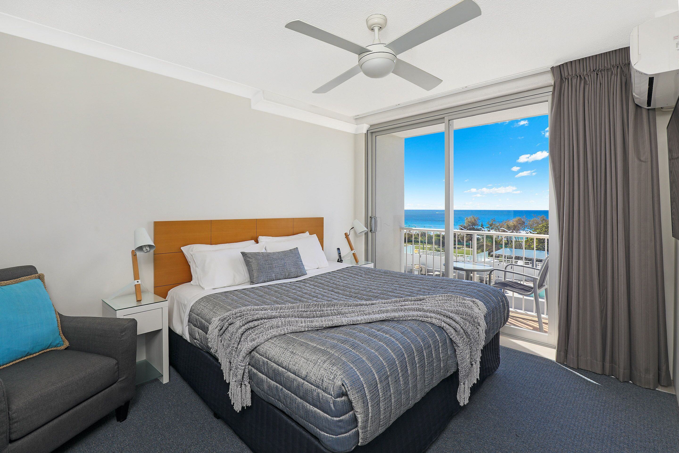 A hotel room with a bed, a nightstand, a chair, a ceiling fan, and a balcony with a view.