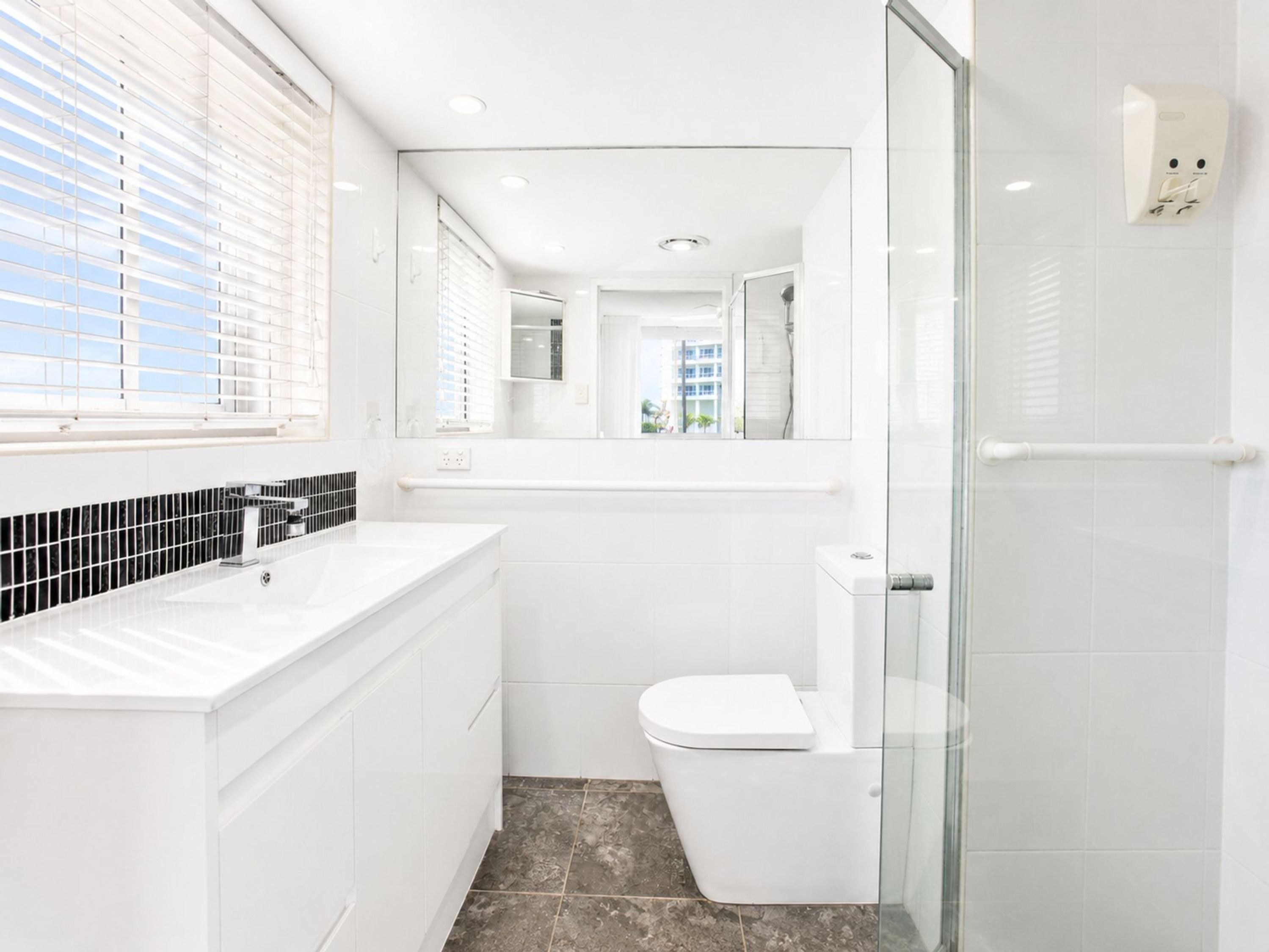 Une salle de bain moderne avec une douche à parois de verre, des toilettes blanches et un meuble-lavabo avec un pare-feu en carreaux noirs.