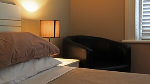 Una habitación de hotel con cama, una silla, una lámpara y una ventana con persianas.