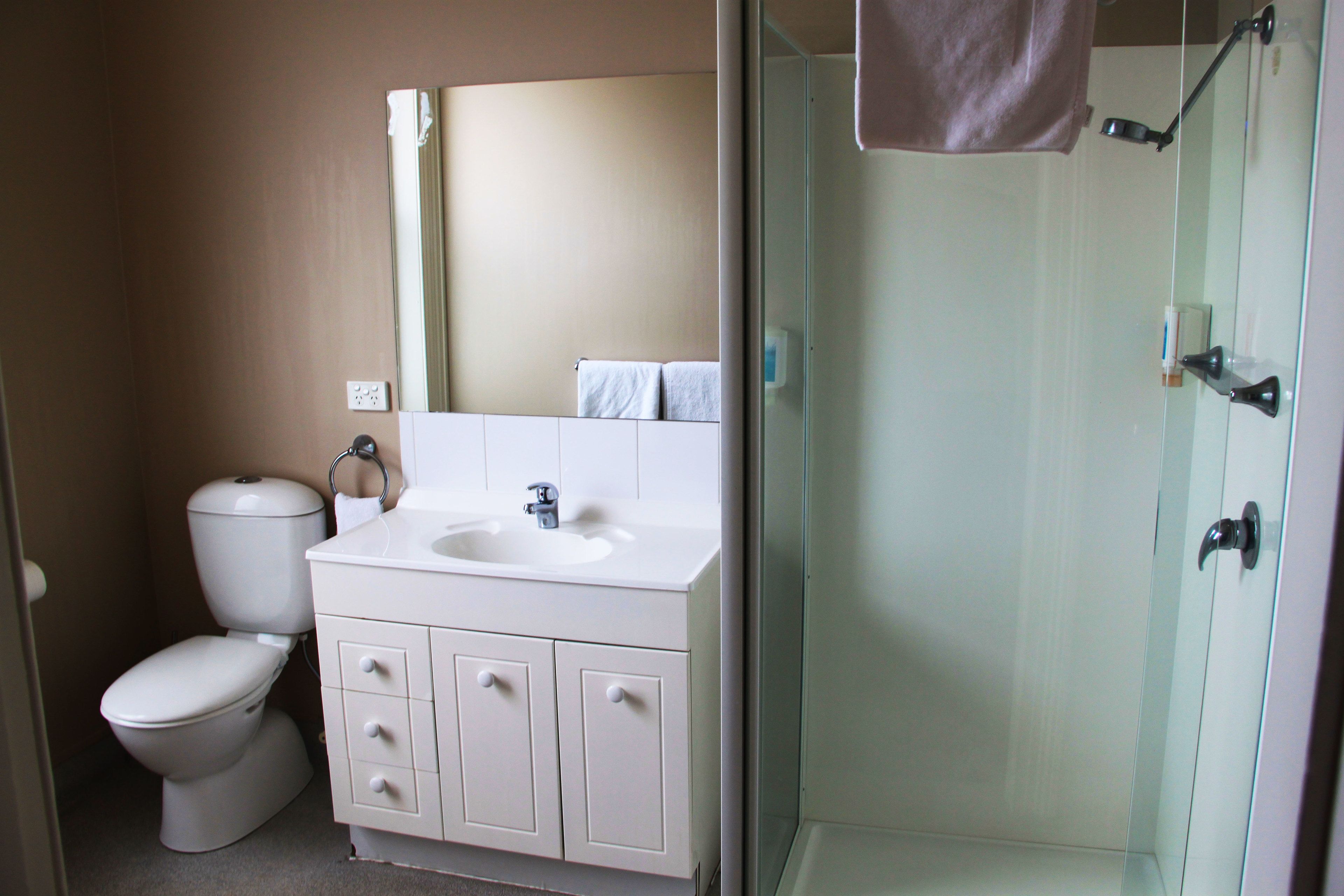 Baño con inodoro, lavamanos y cabina de ducha de vidrio.