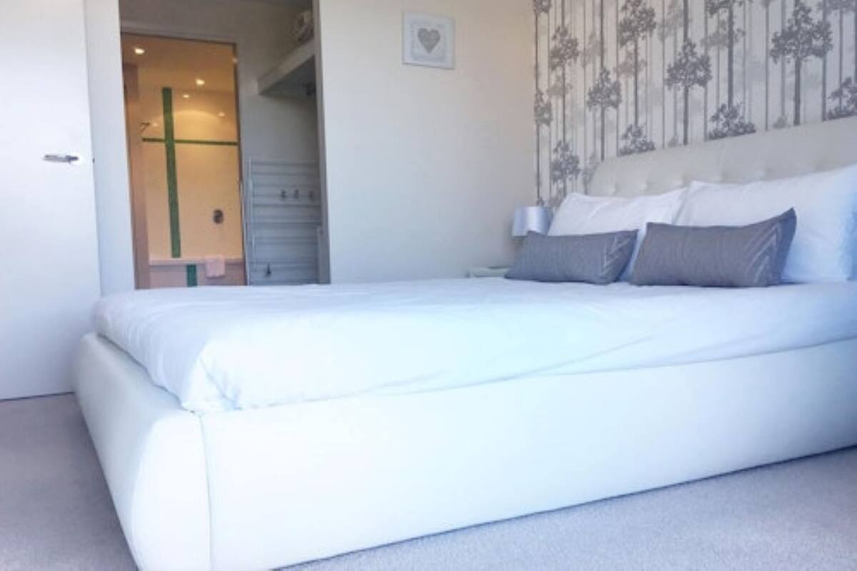 Ein Schlafzimmer mit einem großen Bett, einem Nachttisch, einer Wandleuchte und einer Tür zum Badezimmer.