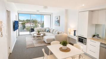 Un appartement moderne comprenant un espace de vie, un coin repas, une cuisine et de grandes fenêtres offrant une vue sur la ville.