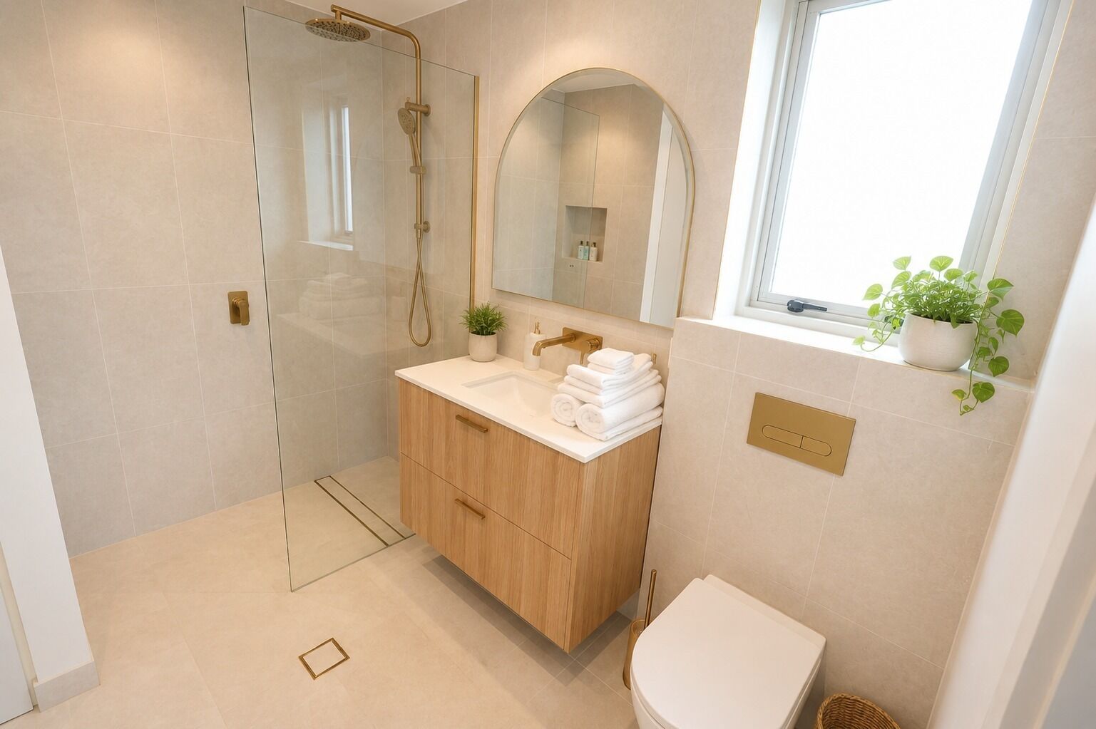 A modern bathroom with a glass-enclosed shower, a wooden vanity, a toilet, and a window with a plant.