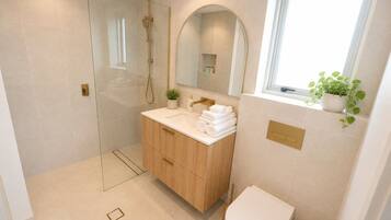 A modern bathroom with a glass-enclosed shower, a wooden vanity, a toilet, and a window with a plant.