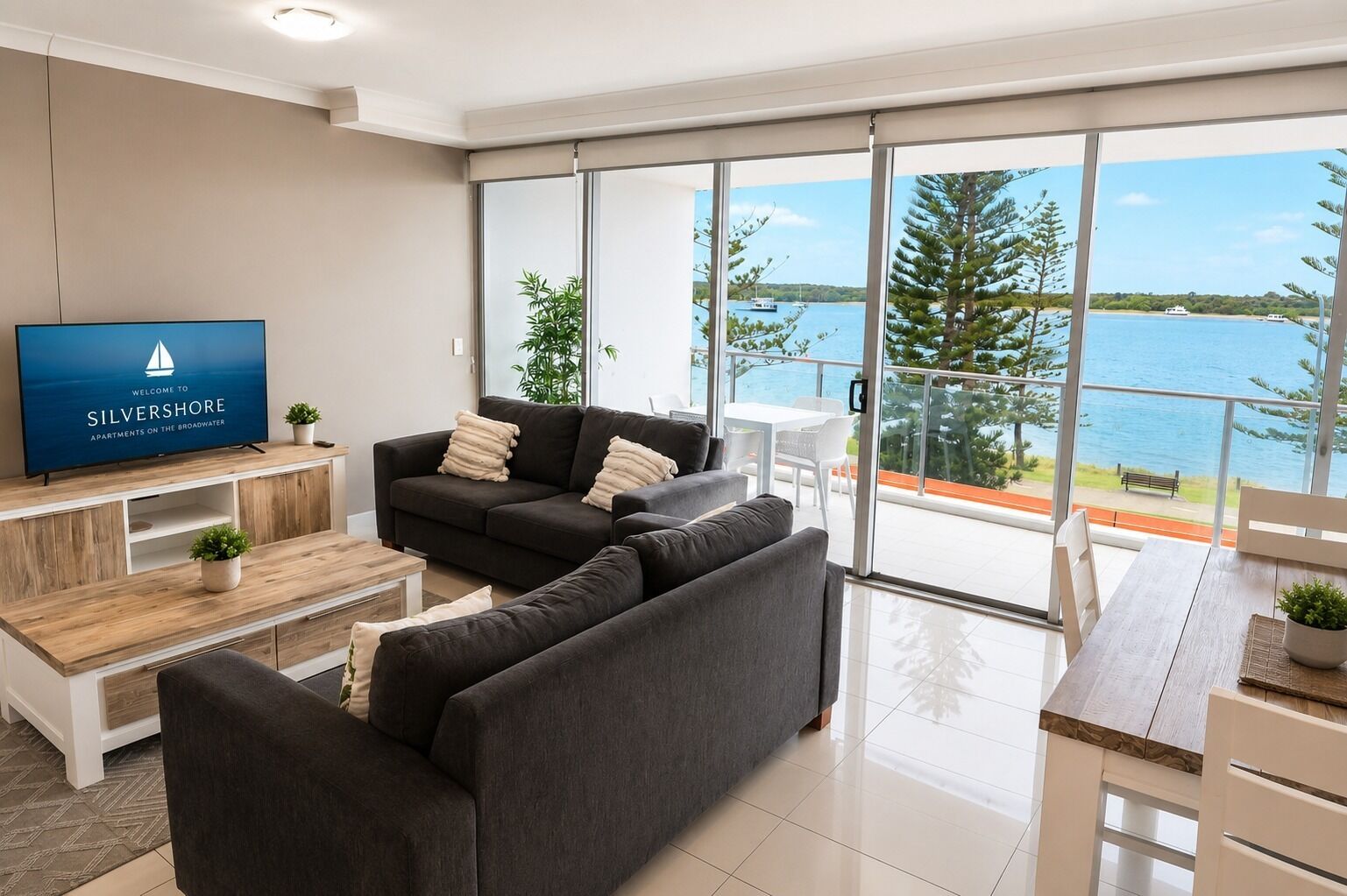 Una sala de estar moderna con un amplio ventanal con vistas a un cuerpo de agua, un televisor de pantalla plana y un conjunto de sofás.