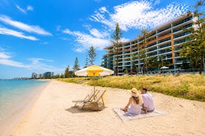 A beach with a sandy shore, a yellow umbrella, and a building with multiple balconies in the background.
