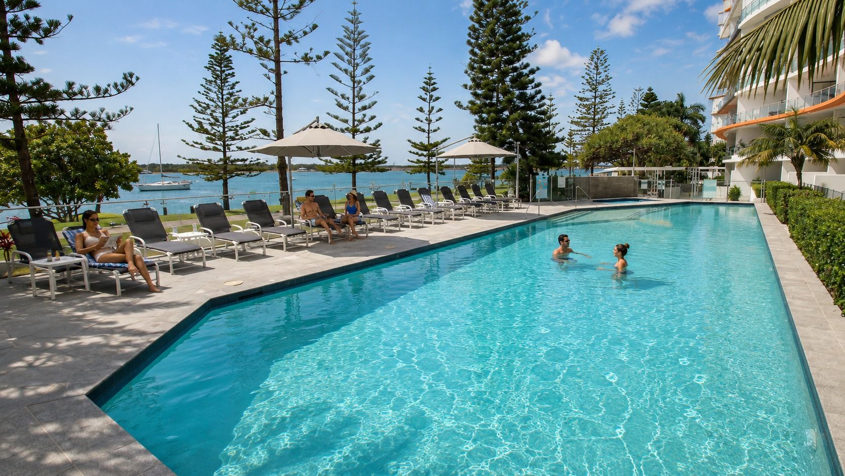 A swimming pool with lounge chairs and umbrellas, surrounded by trees and a view of the sea.