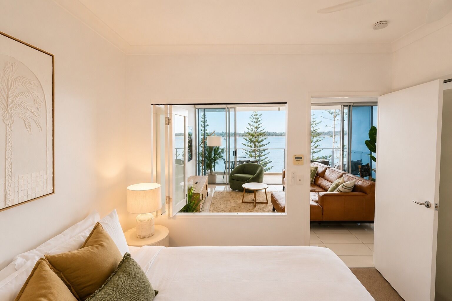 Une chambre d’hôtel comprenant un lit, un coin salon avec un canapé et un fauteuil, ainsi qu’un balcon offrant une vue sur la mer et les arbres.