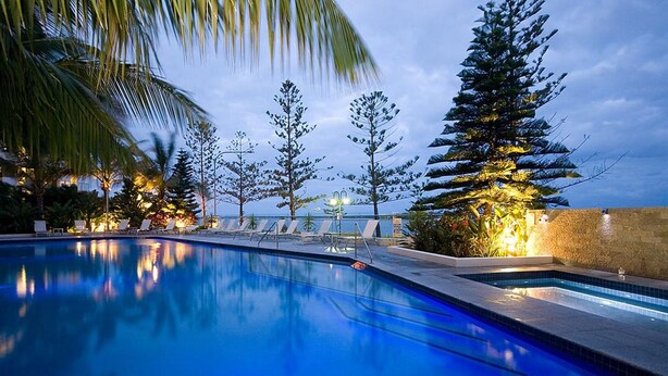 Une piscine entourée d’un mur de pierre et de palmiers, agrémentée de chaises longues et de plantes tropicales.