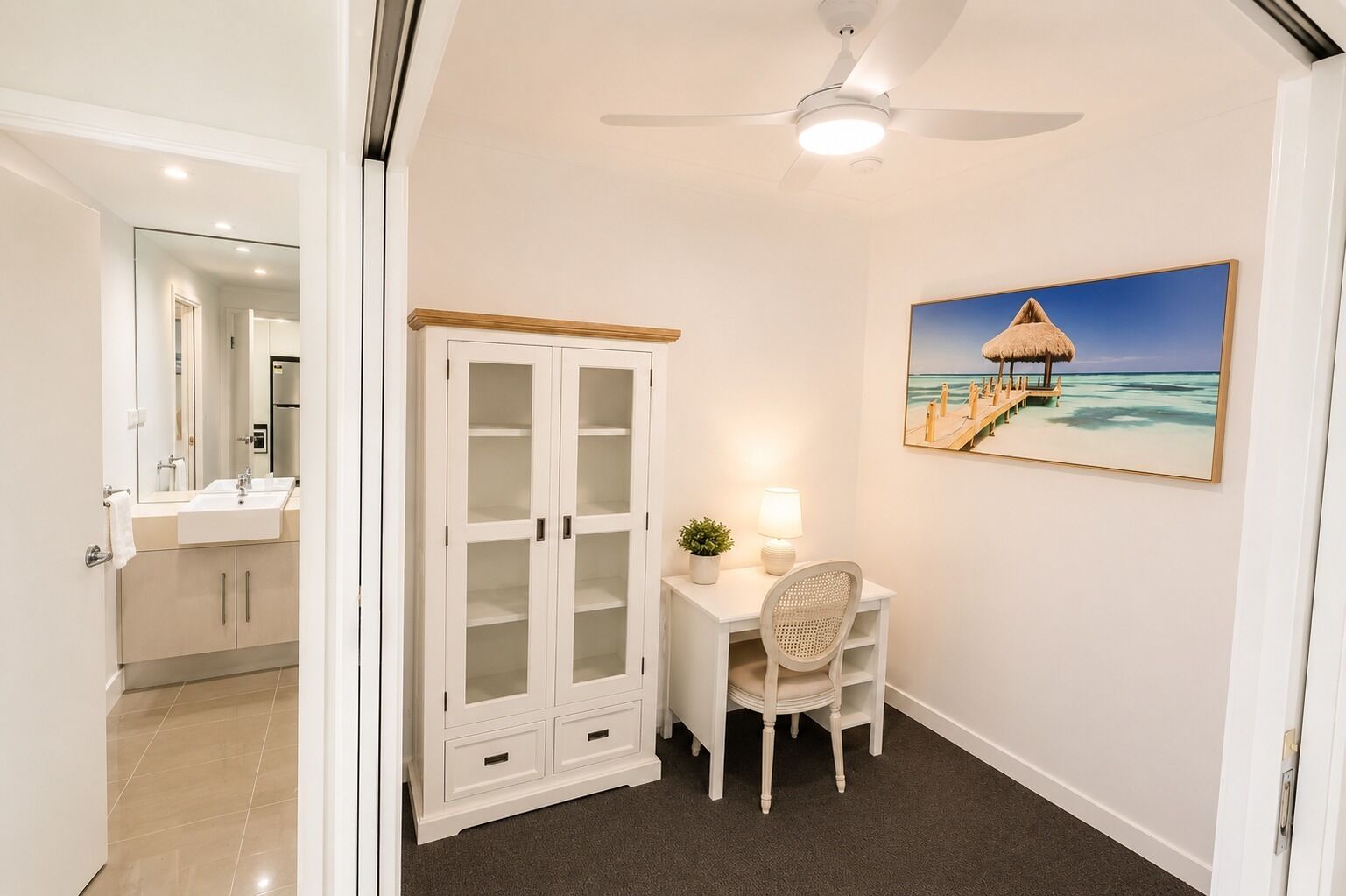Une pièce comprenant un bureau, une chaise, un meuble et un tableau représentant une scène de plage.