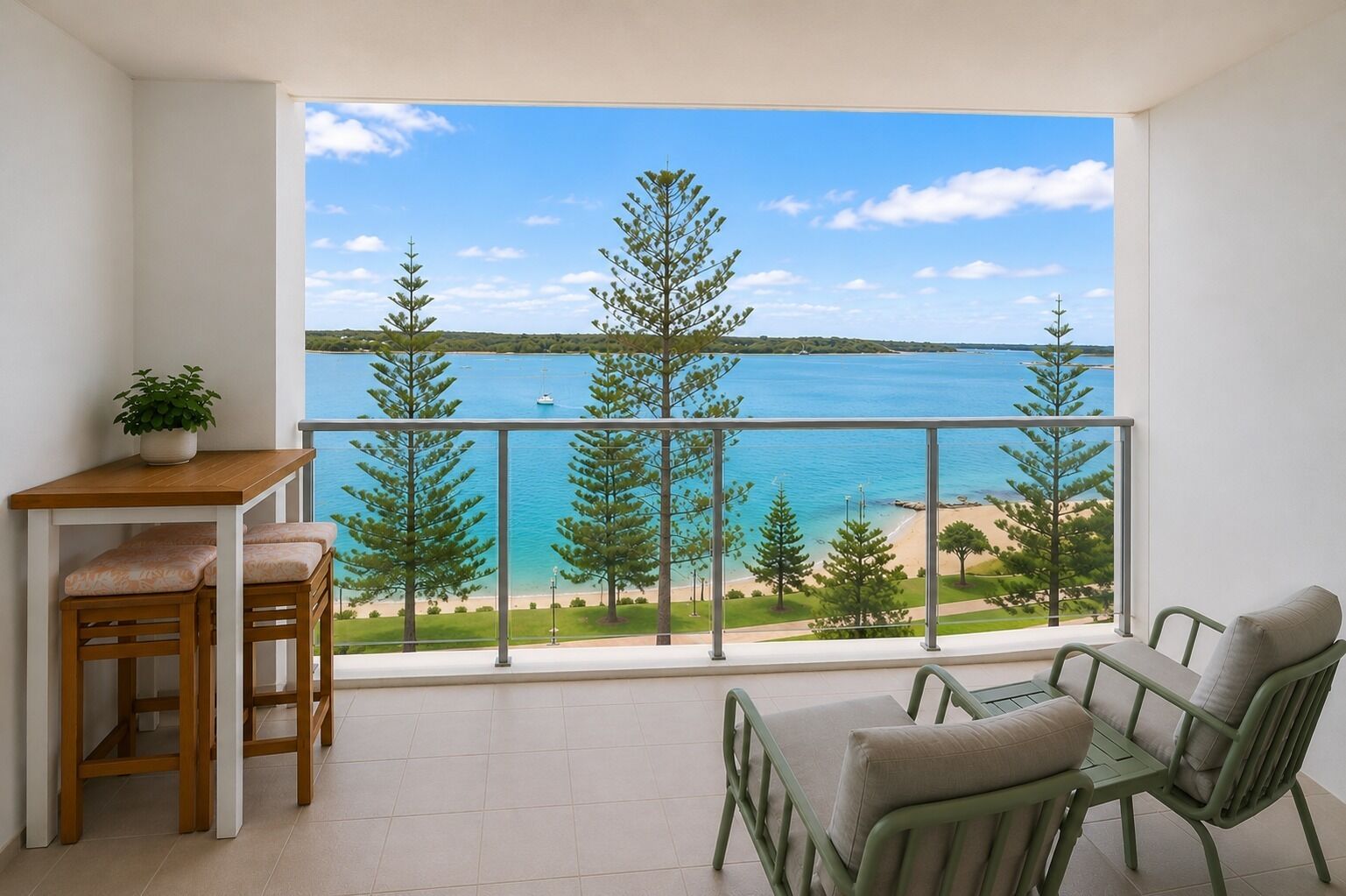 A balcony with a view of a beach and the sea, furnished with a table and chairs.