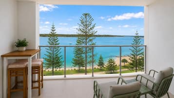 A balcony with a view of a beach and the sea, furnished with a table and chairs.