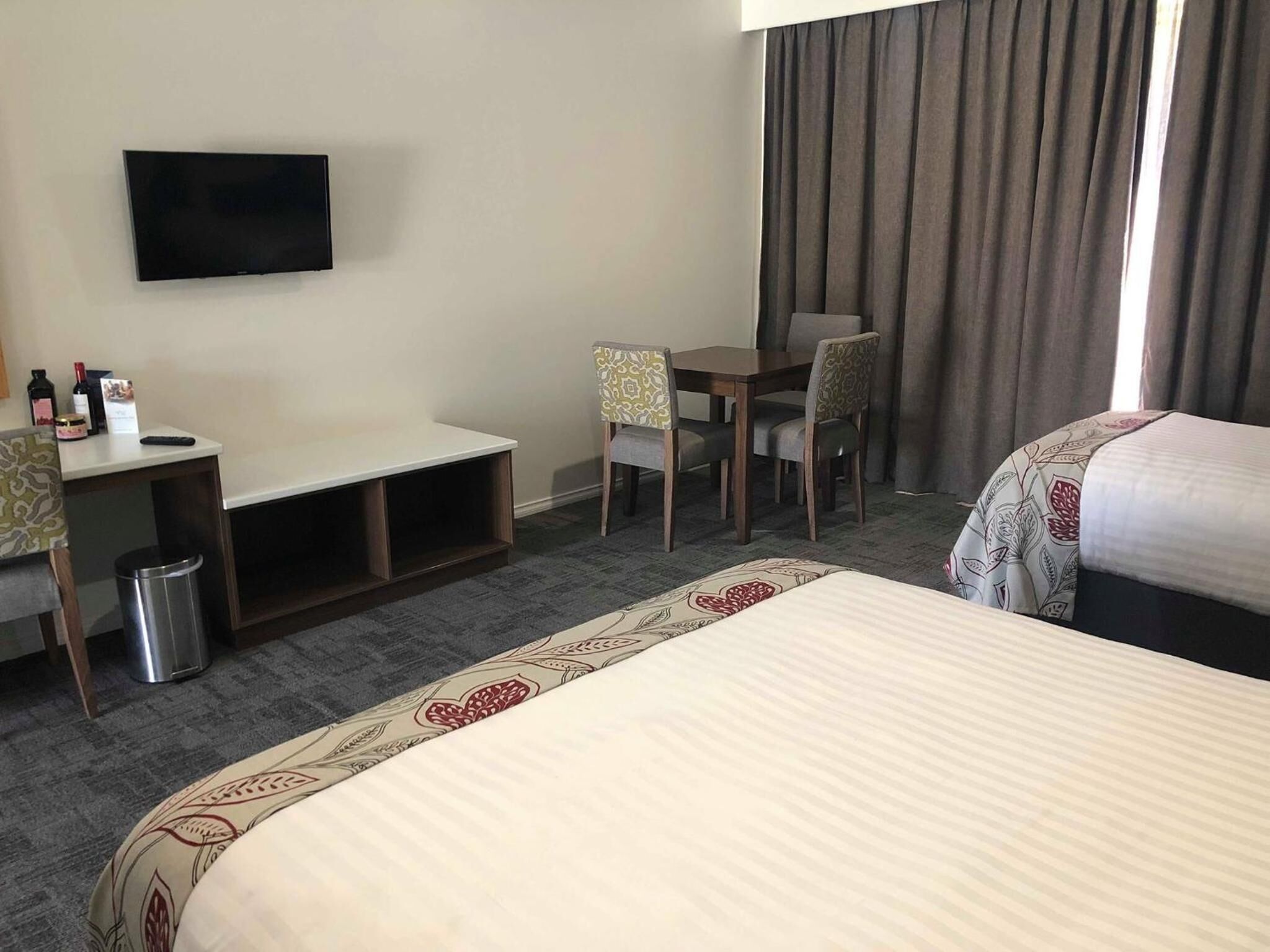 Habitación de hotel con cama, escritorio, silla, televisor y un pequeño cubo de basura.