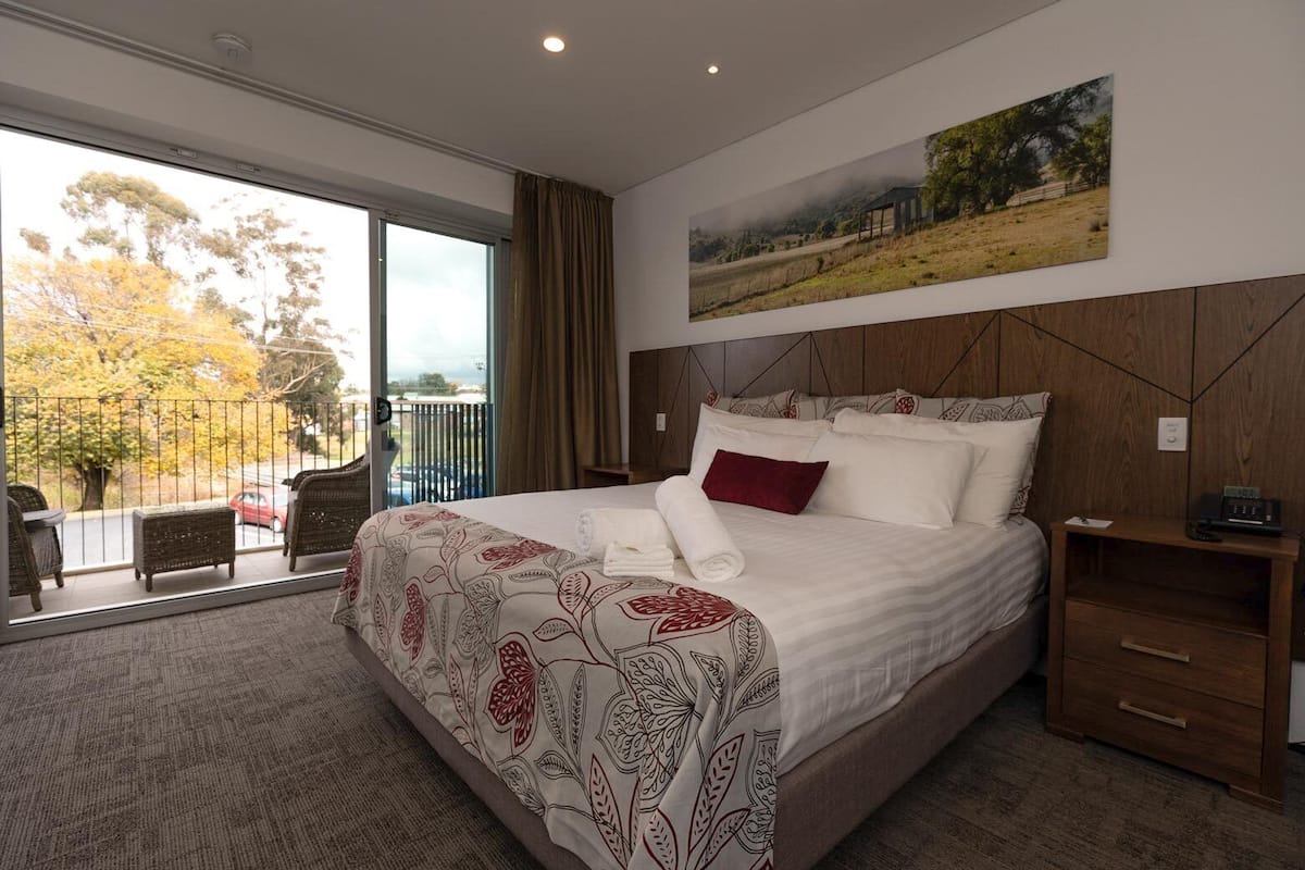 Une chambre spacieuse avec un grand lit, une tête de lit en bois, une table de chevet et une vue sur l’extérieur grâce à une porte-fenêtre coulissante.