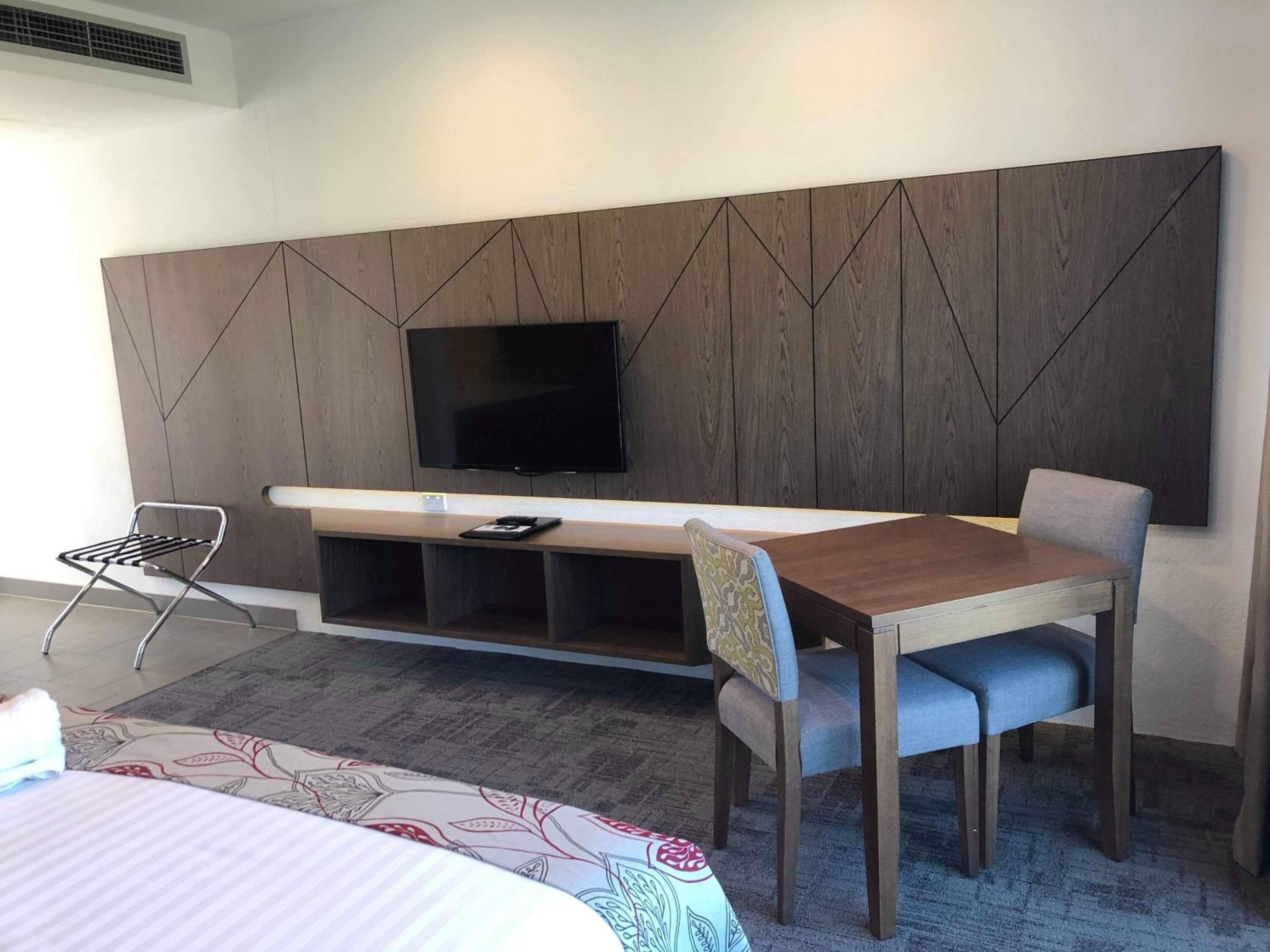 Ein Hotelzimmer mit Bett, Schreibtisch mit Stuhl, Fernseher und einer kleinen Ablagefläche.
