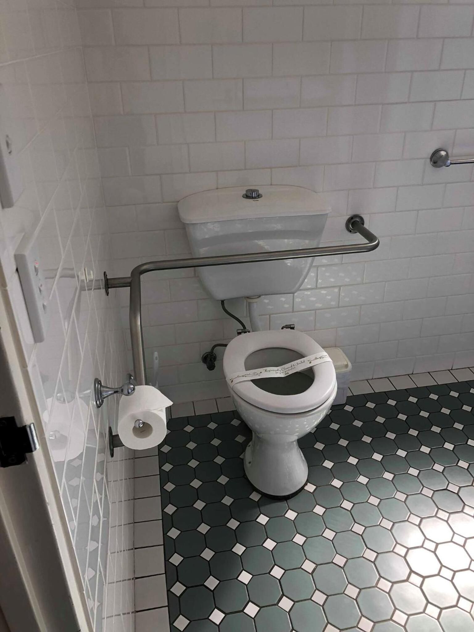 A bathroom with a white toilet, a handrail, and a hexagonal patterned floor.