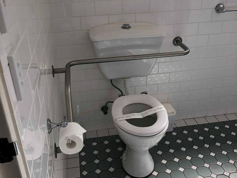 A bathroom with a white toilet, a handrail, and a hexagonal patterned floor.