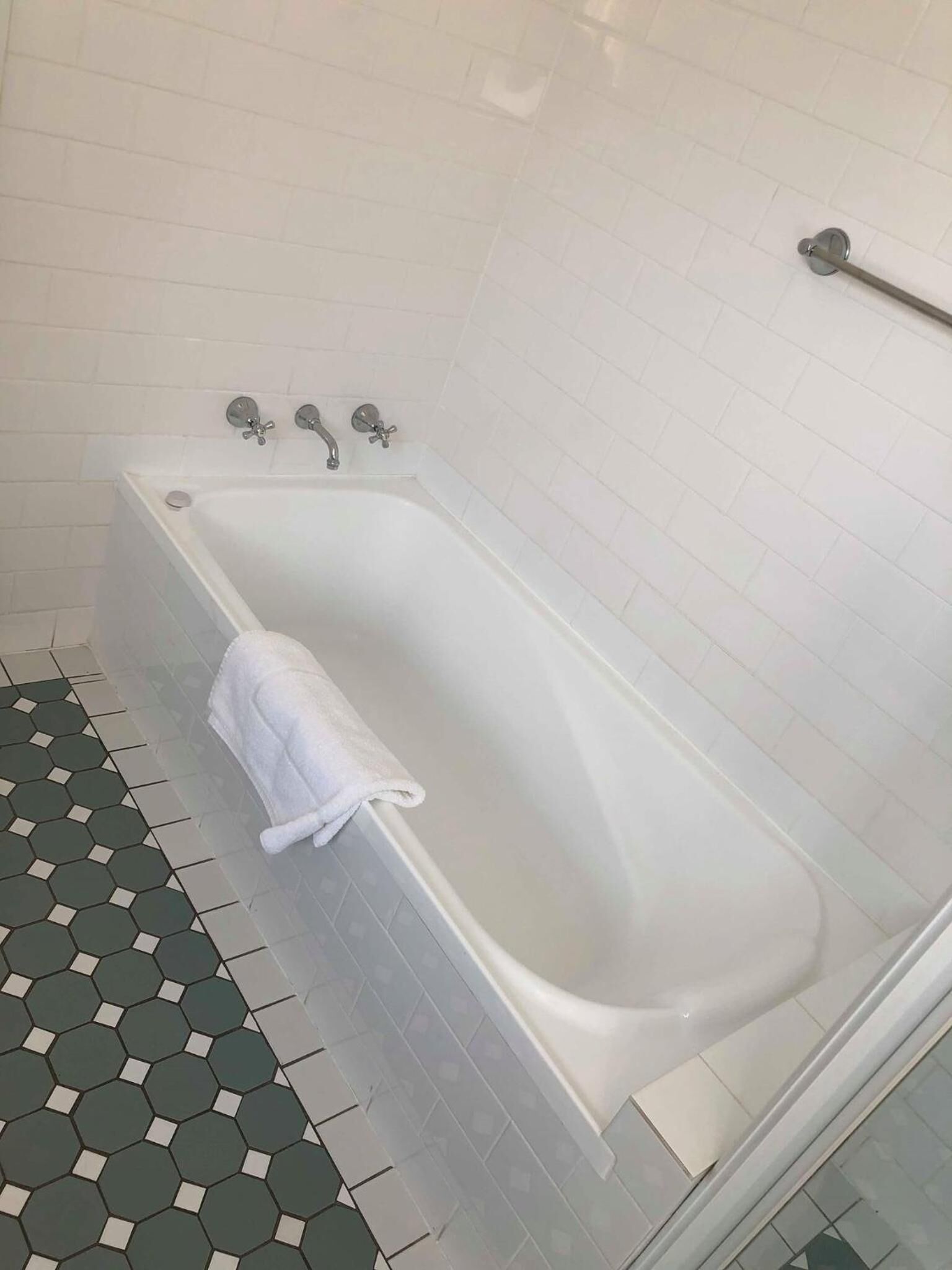 Un baño con una bañera blanca, una toalla y un suelo de baldosas hexagonales.