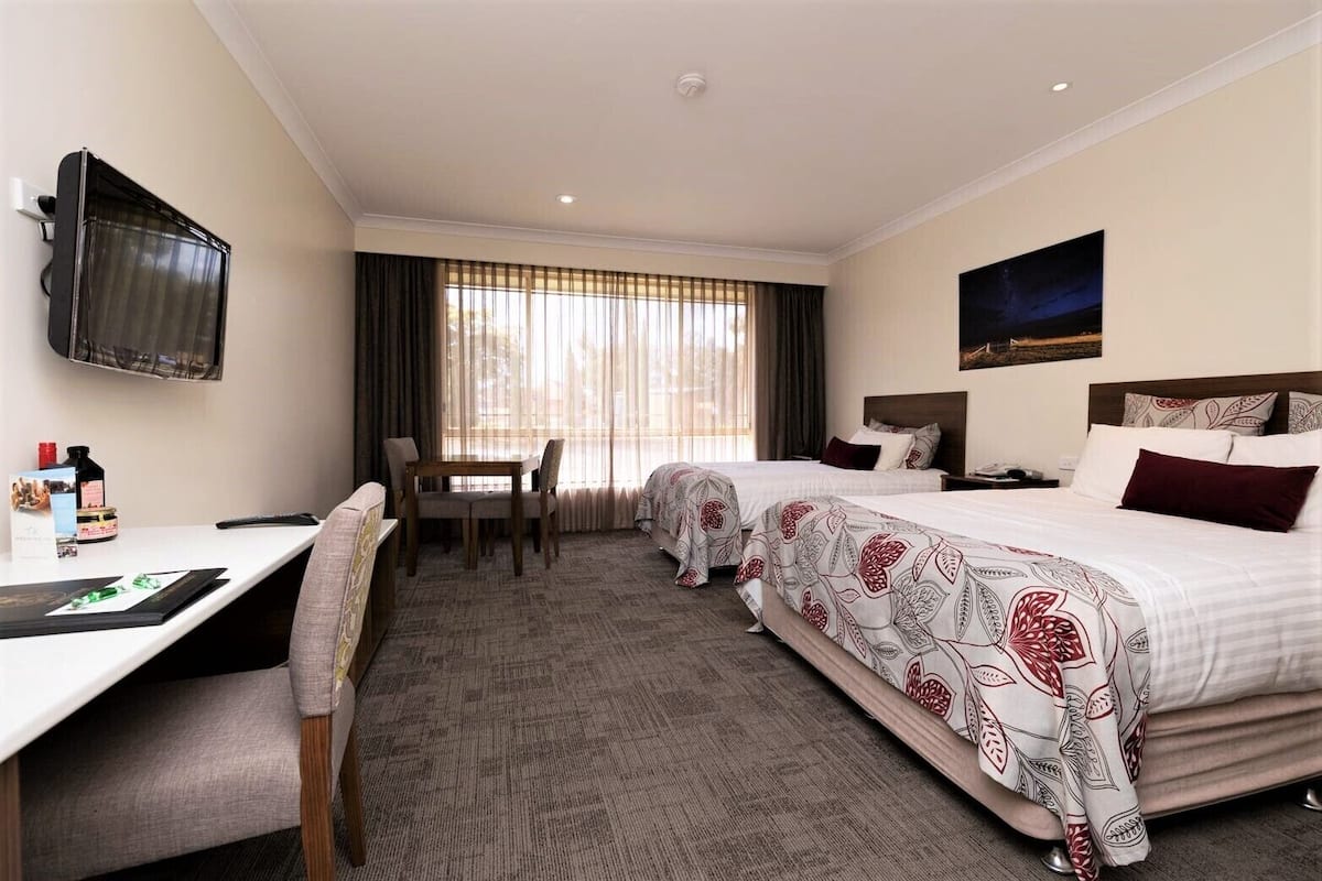Une chambre d’hôtel avec deux lits, un bureau, une chaise, une télévision et une fenêtre avec des rideaux.