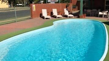 Relax by the pool at Motor Inn, surrounded by lush greenery and comfortable lounge chairs.