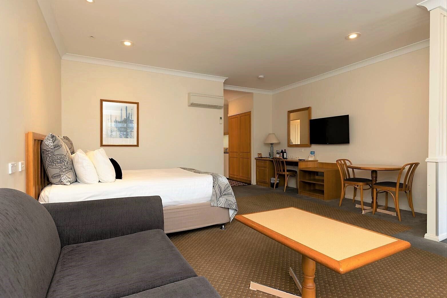 Una habitación de hotel con cama, sofá, escritorio con silla, televisor y equipo de aire acondicionado.