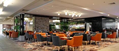 Un moderno vestíbulo de hotel con área de bar, asientos y plantas decorativas.
