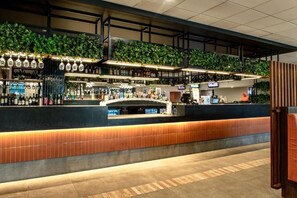 Una zona de bar con mostrador, estantes llenos de botellas y plantas colgantes.