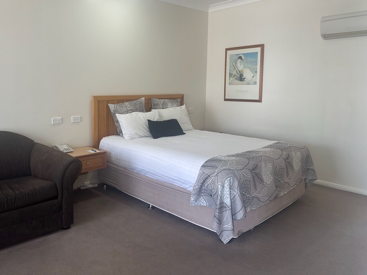 A bedroom with a bed, a bedside table with a phone, a brown couch, and a framed picture on the wall.