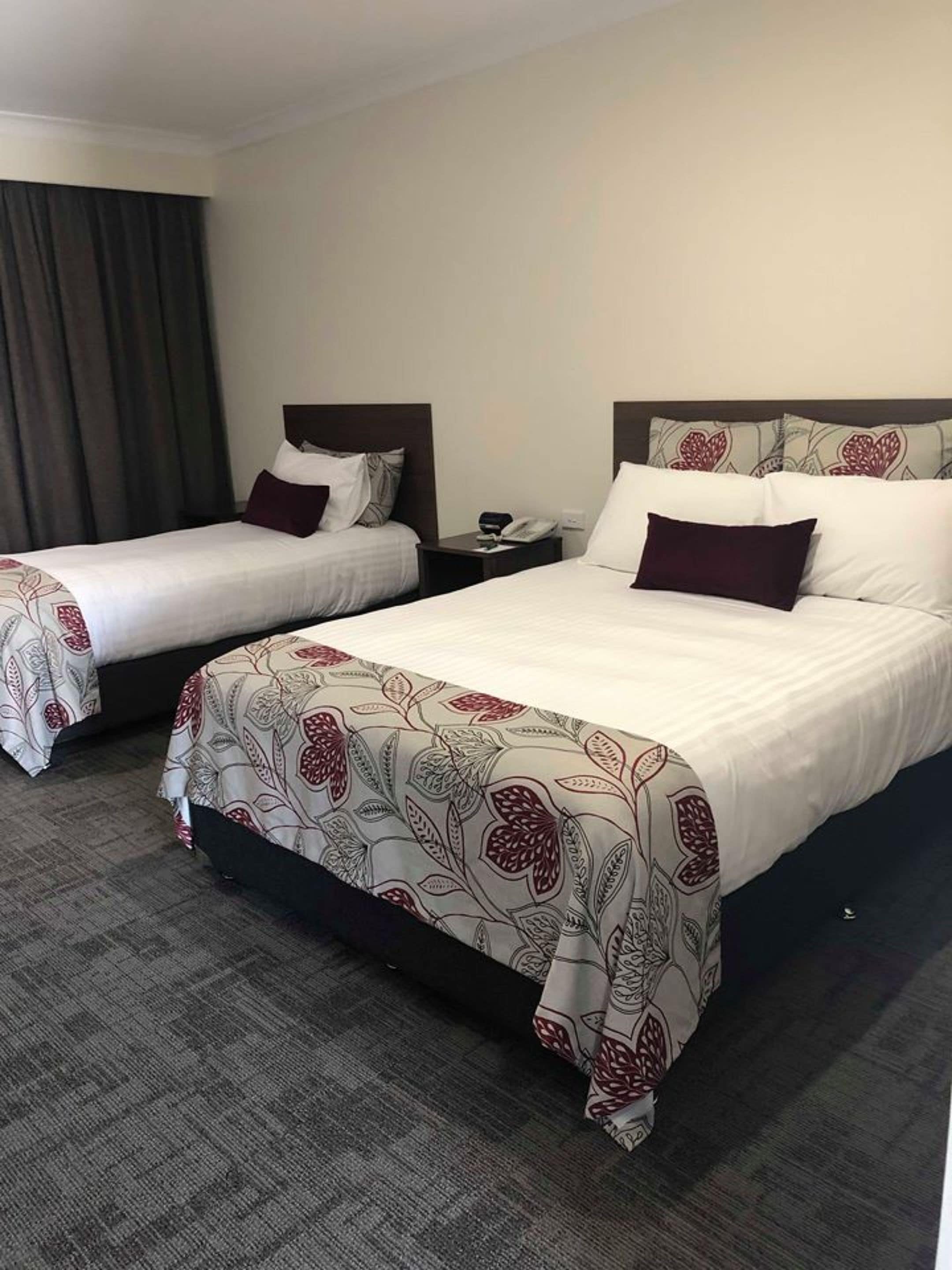 Two single beds with dark headboards, a grey carpet, and a patterned bedspread.