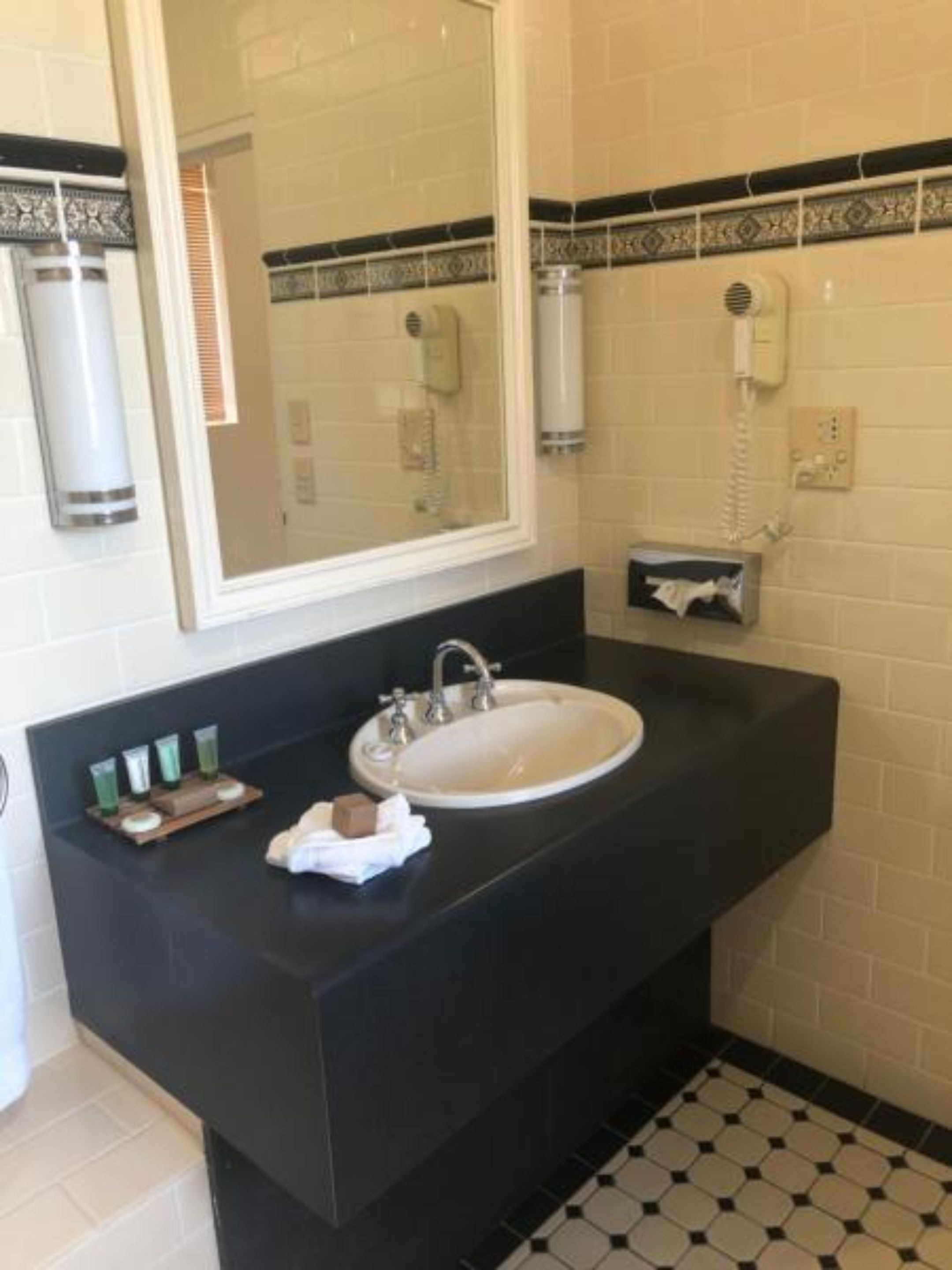 A bathroom with a white sink, black countertop, and a mirror above it. There are toiletries on the counter and a towel hanging on the wall.