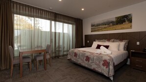 A hotel room with a large bed, a dining table with chairs, and a painting on the wall. - Young Federation Motor Inn (Young)