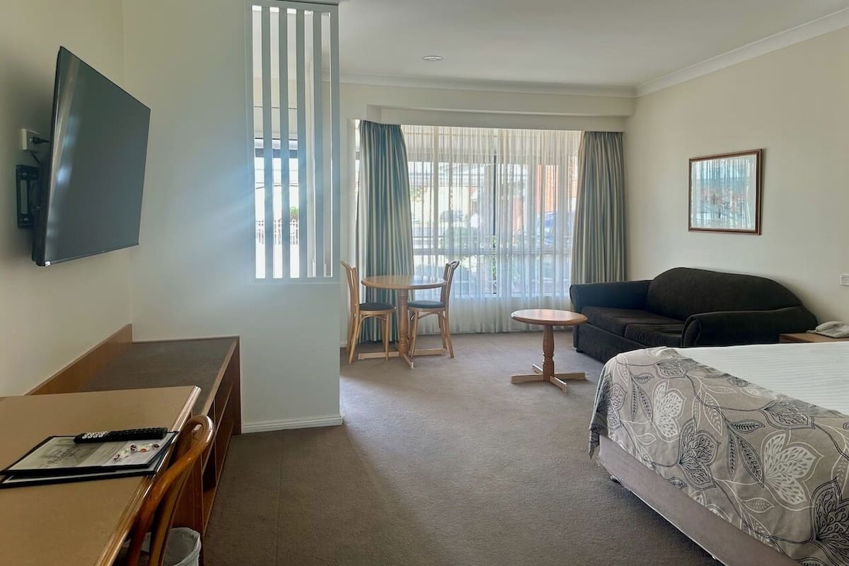 Une chambre d’hôtel équipée d’un lit, d’un bureau, d’une chaise, d’une petite table, d’un canapé et d’une télévision.