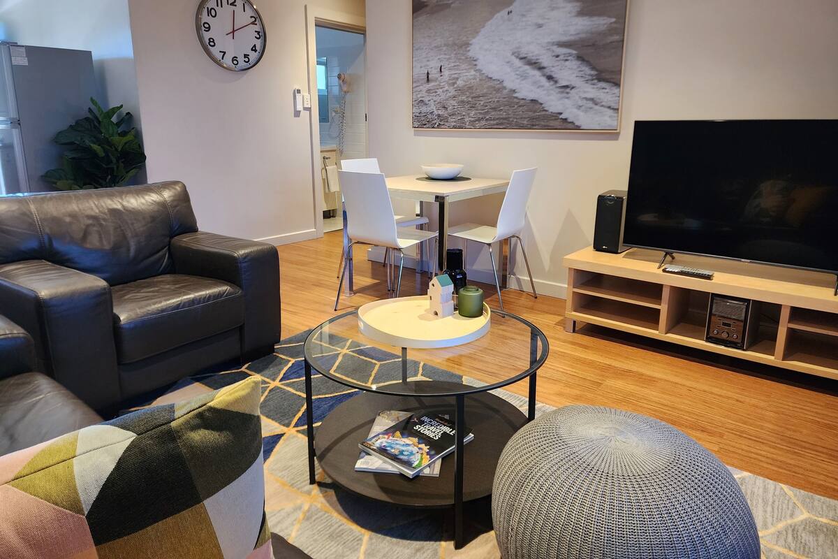 A modern living room with a leather sofa, a round coffee table, a TV, and a dining area with a white table and chairs.