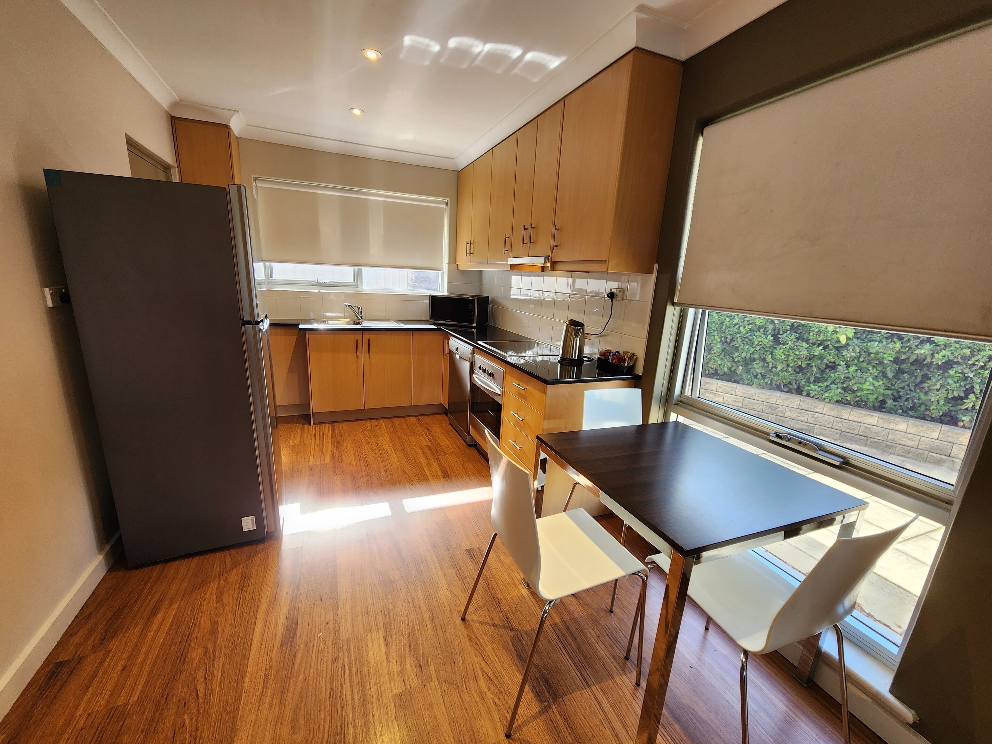 A modern kitchen with wooden cabinets, a black refrigerator, a sink, and a window overlooking greenery.