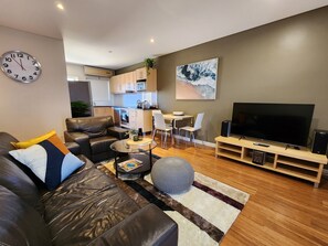 A modern living room with a leather sofa, a glass coffee table, a TV, and a dining area with chairs and a table. - Ethelton Serviced Apartments (Ethelton)